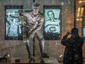 A man takes a photo of an illuminated statue of Canadiens legend Jean Béliveau outside the Bell Centre in Montreal on Dec. 3, 2014, the day after the Hall of Famer died at age 83.