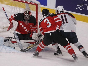 Team Canada goalie Eric Comrie, stops Team USA Miles Wood (11), who's being check closely by Dilon Heatherington (3), during first period preliminary round hockey action at the IIHF World Junior Championship in Montreal on Wednesday December 31, 2014.