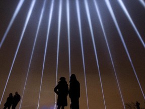 A couple stands in silhouette against some of the 14 beams of light pointing skywards in memorial of the victims of the Polytechnique shooting at the Mont Royal Chalet in Montreal, Dec. 6, 2014.