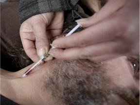 Martin Paré holds his shirt out of the way so fellow drug addict Éric can inject him in the neck with morphine hydrochloride in Viger Square in Montreal Tuesday Nov. 25, 2014.