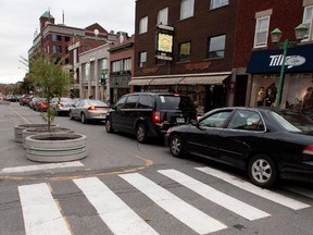 A car is kept to a single lane with the aid of large concrete flower pots, on Laurier street in the Plateau Mont Royal district of  Montreal.