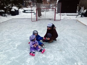 Violet Connell, 2, and brother Jack, 4,  test the ice on a neighbour's rink in Montreal West December 24, 2014 as their mother Kate Shingler helps with laces. (Rene Bruemmer / Montreal Gazette)