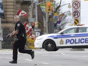 In this Wednesday, Oct. 22, 2014 file photo, an Ottawa police officer runs with his weapon drawn outside Parliament Hill in Ottawa, where Michael Zehaf-Bibeau killed a soldier outside Canada's parliament.
