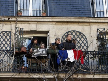 People display a note "Je suis Charlie" (I am Charlie) and a French flag as they watch from a balcony the Unity rally Marche Republicaine in Paris on January 11, 2015 held in tribute to the 17 victims of a three-day killing spree by homegrown Islamists. The killings began on January 7 with an assault on the Charlie Hebdo satirical magazine in Paris that saw two brothers massacre 12 people including some of the country's best-known cartoonists, the killing of a policewoman and the storming of a Jewish supermarket on the eastern fringes of the capital which killed 4 local residents.