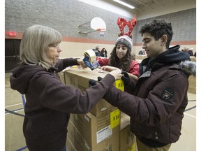 MONTREAL, QUE.: DECEMBER 13, 2014 -- Wendy Gariepy left, of the West Island Mission foodbank  tapes up a christmas basket box after showing its contents at Westview Church in Pierrefonds, helping her and waiting to deliver the boxes to waiting cars are Scouts Celine Naoum middle, and Alexandre Naoum right, Saturday, December 13, 2014. (Peter McCabe / MONTREAL GAZETTE)