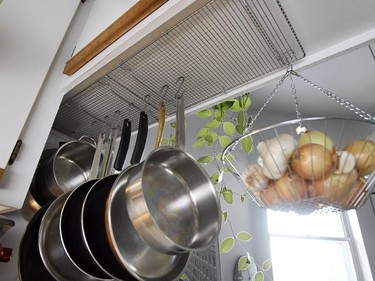 Professional organizer Alison Lush uses inverted cookie cooling racks screwed to the underside of a kitchen cabinet from which she hangs pots and pans and a vegetable basket in her apartment.