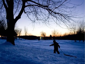 A boy gets in some tobogganing before the sun sets on a snow covered Mount-Royal Park.