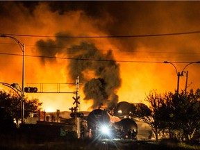 Smoke and fire rises over train cars as firefighters inspect the area after a train carrying crude oil derailed and exploded in the town of Lac-Mégantic, 100 kilometres east of Sherbrooke on Saturday, July 6, 2013.