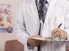 A medical professional writes on a clipboard while standing in a doctor's office.