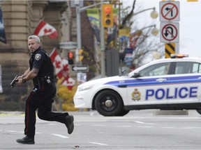 In this Wednesday, Oct. 22, 2014 file photo, an Ottawa police officer runs with his weapon drawn outside Parliament Hill in Ottawa. Radical Muslim Michael Zehaf-Bibeau killed a soldier outside Canada's parliament. Nearly nine out of 10 Quebecers support the Harper government’s anti-terror bill, a new poll shows.