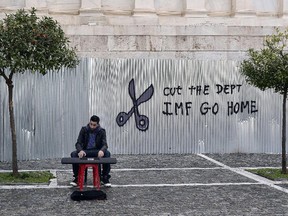 A man plays music on a digital keyboard near graffiti on a corrugated metal gate reading "Cut the debt, IMG go home" in Athens on February 24, 2015. Greece edged closer to eurozone survival on February 24 as its international creditors and hold-out Germany looked ready to approve the reforms they had demanded of Athens in return for extending its bailout programme.