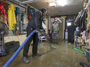 Water damage technician Dany Visante, left, helps Antonio Cruz vacuum water from Cruz's flooded basement after a water main ruptured on 16th Avenue just south of Masson, in Montreal, Tuesday February 10, 2015.