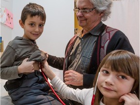 Pediatrician Gilles Julien looks on as 8-year-old Océane Loutef-Beauchesne listens through the stethoscope to the heartbeat of her brother, 7-year-old  Dylan, during the family appointment.