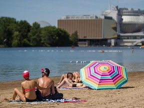 A couple applies sunscreen with the Montreal Casino in the background at the beach at Jean-Drapeau Park in Montreal on Sunday, June 15, 2014.