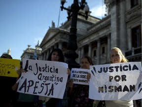 Women holds sign that reads in Spanish; "Argentine justice stinks," second left, "and "Justice for Nisman," right, during a march for justice and against impunity in the case of the mysterious death of late prosecutor Alberto Nisman, in Buenos Aires, Argentina, Wednesday, Feb. 4, 2015.  Investigators examining the death of Nisman, who accused Argentine President Cristina Fernandez of agreeing to shield the alleged masterminds of a 1994 terror bombing, said Tuesday, they have found a draft document he wrote requesting her arrest.
