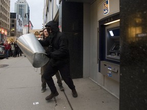 A masked protestor tries to break an RBC ATM on Ste-Catherine St. during an anti-police brutality demonstration in Montreal, Thursday, March 15, 2012.