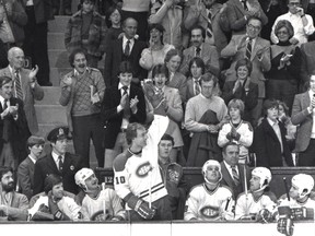 Montreal Canadiens star Guy Lafleur waves from the Canadiens bench to acknowledge a Montreal Forum standing ovation on March 4, 1981 after registering his 1,000th career NHL point. In the front row of fans behind Lafleur, in a dark sports jacket just to the left of Lafleur's raised gloved hand, is 15-year-old future NHL great Mario Lemieux, then a Midget Triple-A superstar with Montreal-Concordia. Canadiens on the bench, from left: goalie Denis Herron and forwards Pierre Mondou, Lafleur, Pierre Larouche, Keith Acton and the late Doug Wickenheiser. Just behind Lafleur is assistant trainer Pierre Meilleur; between Larouche and Acton is Habs head coach Claude Ruel.