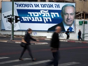 Israelis walk past by campaign posters showing Israeli Prime Minister and Likud party's candidate running for general elections, Benjamin Netanyahu on March 12, 2015 in the central Israeli city of Ramat Gan. Israelis vote on march 17, 2015 in an election seen as a referendum on the tenure of Netanyahu, who could lose but still secure a new term in power.