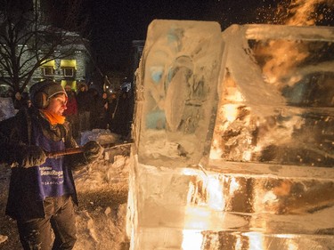 Meliniege Beauregard works on an ice sculpture as a fire burns on the interior of the structure in Old Montreal during Nuit Blanche on Saturday, Feb. 28, 2015.