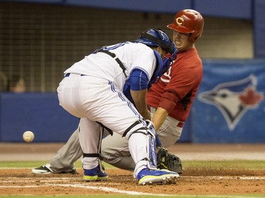 Cincinnati Reds' Jim Riggleman scores past Toronto Blue Jays catcher Dioner Navarro on a hit by Reds' Skip Schumaker during eight inning Grapefruit League action Friday, April 3, 2015, in Montreal.
