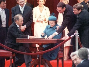 Queen Elizabeth II signs Canada's constitutional proclamation in Ottawa on April 17, 1982 as Prime Minister Pierre Trudeau looks on. Michael Pitfield in glasses is showing Queen Elizabeth where to sign the document.