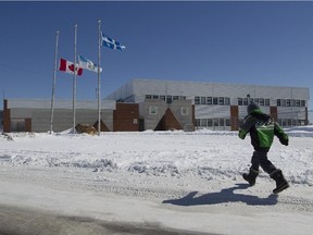 A child runs past Voyageur Memorial High School in Mistissini, a Cree village north of Montreal, Saturday, April 4, 2015, as flags fly at half staff to honour the five men from the village who perished earlier in the week in a cabin fire north of the village.