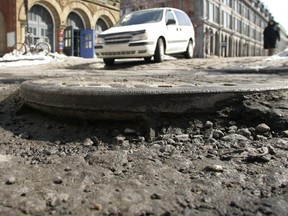 A car drives by a pothole where a manhole cover is left exposed from erosion, at the intersection of Place d'Youville and St Pierre street in Old Montreal.