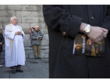 A priest looks on as the Way of the Cross participants participate in a group prayer outside Notre Dame Basilica, Friday April 3, 2015.