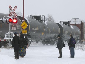Passengers wait for a freight train to pass before crossing the tracks to catch the AMT commuter train, at the AMT station in Baie d'Urfé, Montreal, Thursday December 11, 2014.