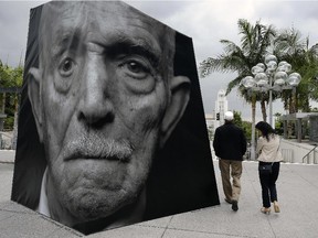 A couple walk past an outdoor installation called iwitness, a grouping of 20 larger-than-life 3-D photo sculptures of Armenian genocide survivors, at the Music Center Plaza in downtown Los Angeles on Friday, April 24, 2015.