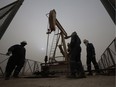 Men work on an oil pump during a sandstorm in the desert oil fields of Sakhir, Bahrain.
