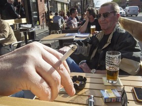 The hand and cigarette of Jeffrey Cox rests on the handrail of a outdoor terrasse at the Burgundy Lion pub, while his friend John Carley, right, also enjoys the same on Tuesday May 5, 2015.