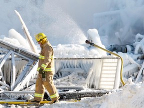 Firefighterwalks past a hose pouring water on the smouldering remains of a seniors residence in L'Isle-Verte on Jan. 23, 2014.