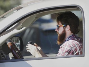 An man works his phone as he drives through traffic.