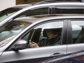 A man uses an iPhone while behind the wheel of a vehicle stopped in traffic at a red light.