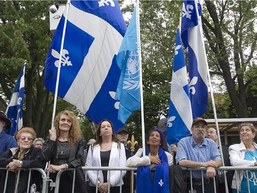 A crowd watches under  Quebec flags across the street from the funeral of former Quebec Premier Jacques Parizeau in Montreal on Tuesday June 09, 2015.