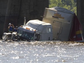 Workers inspect the site where transport truck sits in the Lake of Two Mountains after it went off the Île-aux-Tourtes Bridge on westbound Highway 40 on Friday, June 19, 2015.