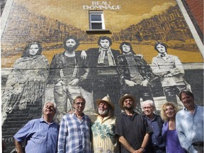 Members of Beau Dommage pose beneath a reproduction of their debut album's cover in the newly named Ruelle Beau Dommage in Rosemont–La-Petite-Patrie, between St-Vallier and St-Denis Sts., near St-Zotique St.