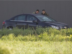 SQ officers examine a car in which two bodies were found, in La Plaine north of Montreal,  June 3, 2015. The windshield appears to have two bullet holes.