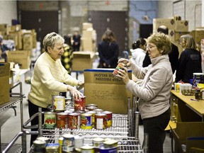 Volunteers Keena Doherty (left) and Danielle Levesque (right) place non-perishable food items in a box for a Christmas food basket at the West Island Mission food warehouse in Pointe-Claire.