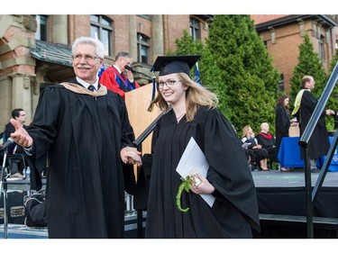 A smiling student, diploma in hand, is helped off the dais by academic staff, at convocation ceremonies held outdoors in front of the Hertzberg Building at John Abbott College in Ste. Anne-de-Bellevue, Quebec on June 11, 2015. Established in 1971, some  2,000 students graduated, with 425 diplomas and honours certificates being awarded.