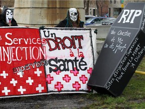 Two masked women hold a banner at press conference by ADDICQ (Association pour la Defense des Droits et l'Inclusion des personnes qui Consomment des Drogues du Québec) under the Jacques Cartier Bridge calling for safe drug injection sites in Montreal Thursday, November 1, 2012.