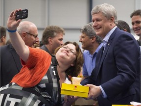 A woman takes a selfie with Prime Minister Stephen Harper as he hands out chicken meals as part of Quebec's Fete Nationale celebrations Wednesday, June 24, 2015 in Sainte-Marie, Que. Minister of Infrastructure, Communities and Intergovernmental Affairs Denis Lebel, right, looks on.
