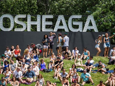 Music fans sit in front of a large Osheaga sign on day one of the 2015 edition of the Osheaga Music Festival at Jean-Drapeau park in Montreal on Friday, July 31, 2015.