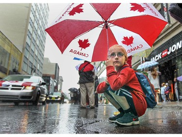 Ian Jones squats under an umbrella as he watches the Canada Day parade make its way down Ste-Catherine St. in Montreal Wednesday July 01, 2015.  Jones and his family are visiting Montreal from Cleveland, Ohio.