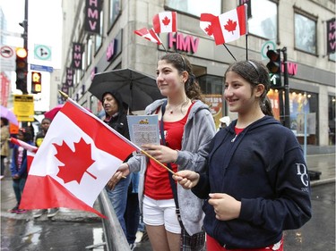 Lauren, left, and Amber Saad were festooned with multiple Canadian flags while watching the Canada Day parade at the corner of  Ste-Catherine St. and Peel in Montreal Wednesday July 1, 2015.