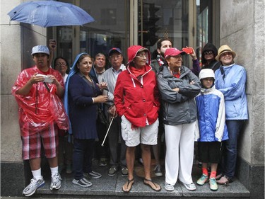 People watch rainy Canada Day parade from the shelter of the entrance to a Ste-Catherine St. store in Montreal Wednesday July 1, 2015.