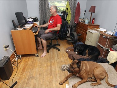 Dominic Caya works on his computer with dogs Bella, rear, and Jax at his side.