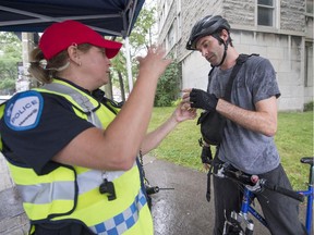 Constable Jocelyn Millette, left, speaks with Ryan Cooney right after giving him a helmet during a bike-safety awareness campaign at the corner of Cherrier and Berri Sts. in Montreal, on Tuesday, July 21, 2015.