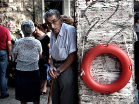 An elderly man stands beside a lifebuoy hanging on a wall outside a chapel in central Athens on July 7, 2015.